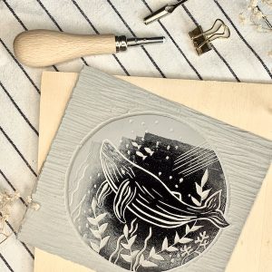 Linoldruckplatte mit Schnitzwerkzeug und Farbrolle, in die das Motiv eines Blauwals geschnitzt ist. Verwendet im Linoldruck Workshop in Köln.