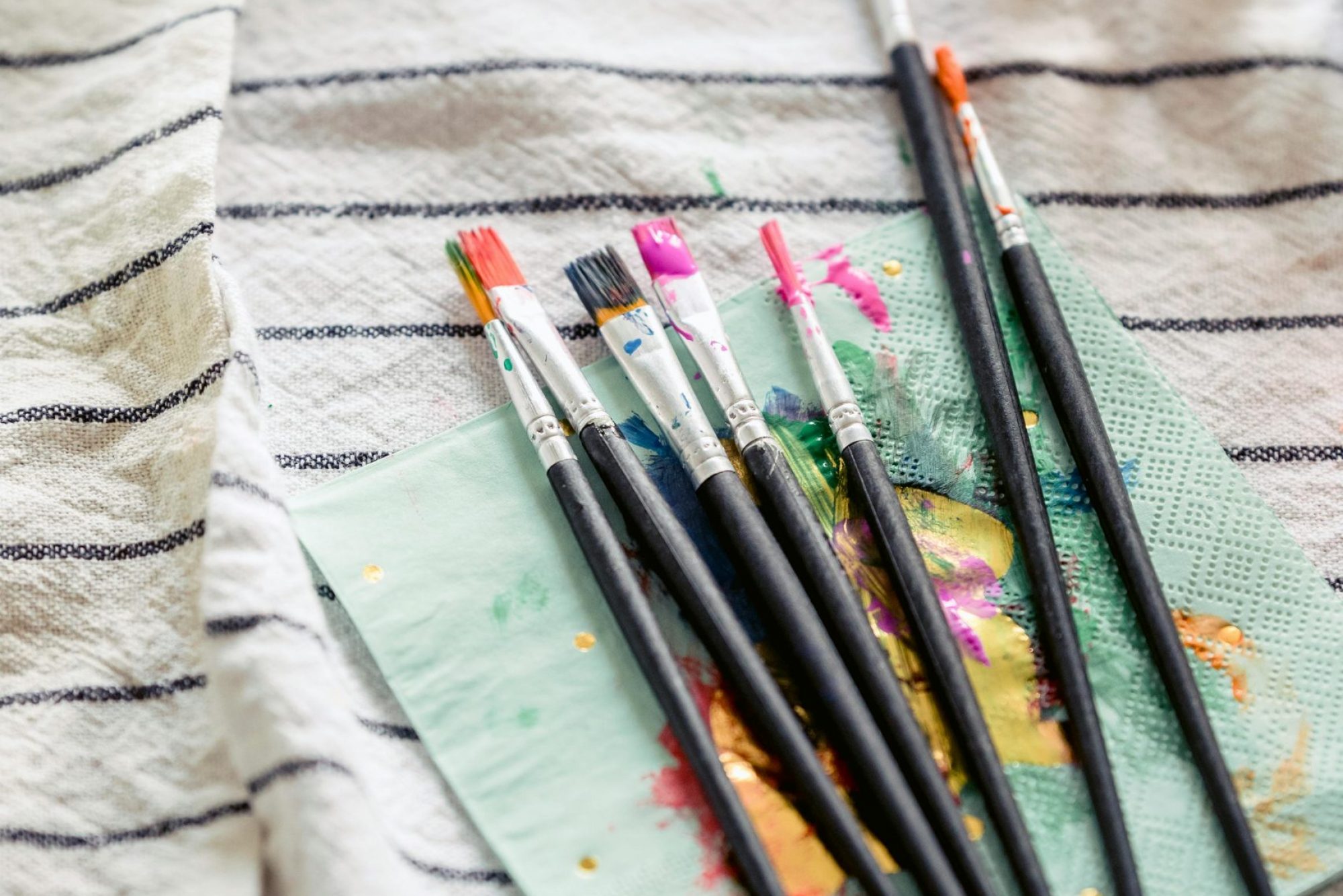 From above collection of paintbrushes on messy napkin on table near colorful paints in light room during Easter holiday preparation